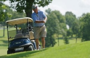 Man Swinging Golf Club with Golf Cart behind him